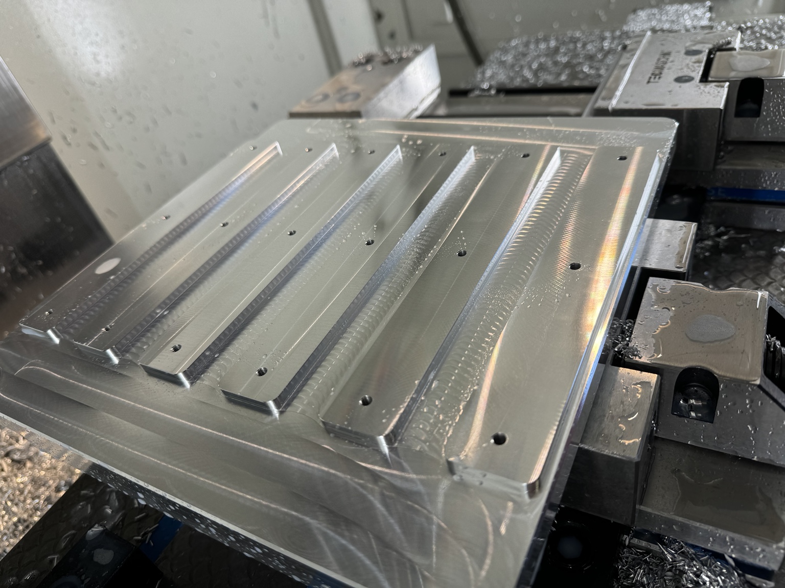 Aluminiumsemne opspændt i CNC-fræseren med fræsede spor og huller.